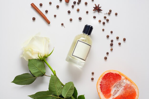 L'olio aromatico è decorato con cannella e una rosa bianca e pompelmo, spezie situate su un muro bianco. il concetto di profumeria, cura del corpo, ingredienti della composizione di oli aromatici.