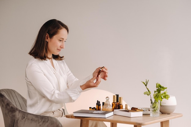 The aromatherapist girl is sitting in her office and holding a bottle of aromatic oils there are essential oils on the table