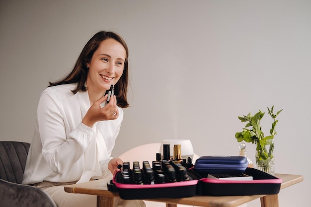 The aromatherapist girl is sitting in her office and holding a bottle of aromatic oils there are essential oils on the table