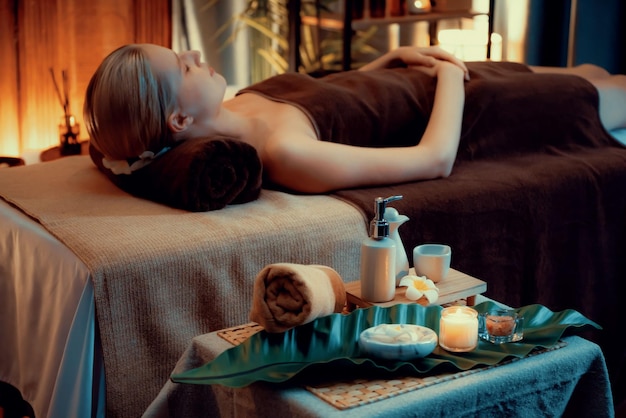 Aromatherapy massage ambiance or spa salon composition setup with focus decor candles and spa accessories on blurred woman enjoying blissful aroma spa massage in resort or hotel background Quiescent