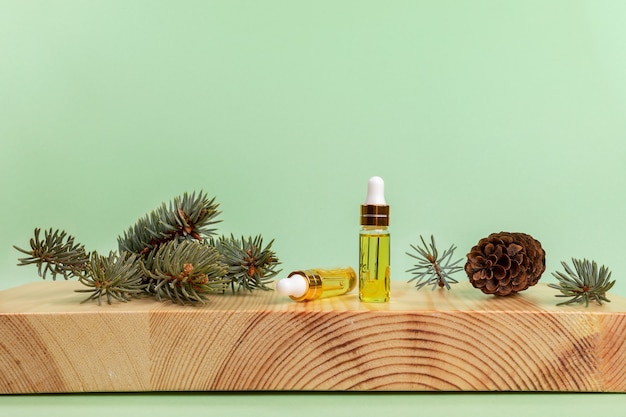 Aromatherapy and spa composition with of essential spruce oil in small glass bottles, green twigs and cone on wooden boxwood stand on light green backdrop. Copy space for text.