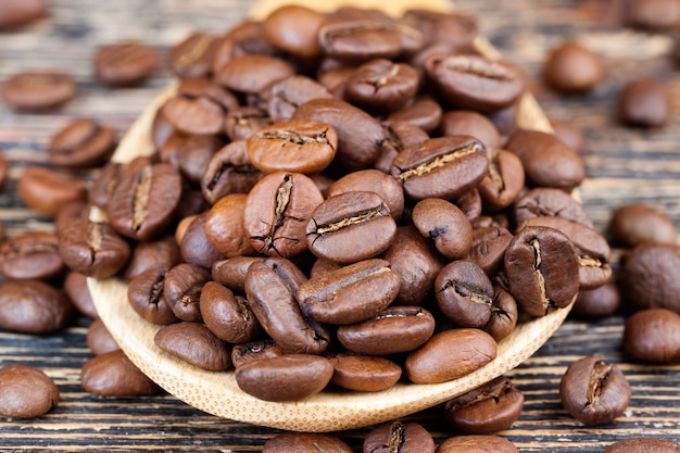 木のスプーンに入った芳香性のコーヒー豆、竹製の計量スプーンでおいしいコーヒーを作るためのコーヒー豆、粉砕用の全体の形のコーヒー豆、クローズアップ