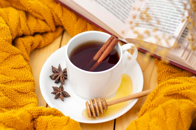 Ароматный горячий чай с корицей, покрытый теплым шарфом на деревянном осеннем фоне. ковшик с медом. комфортно читать книгу