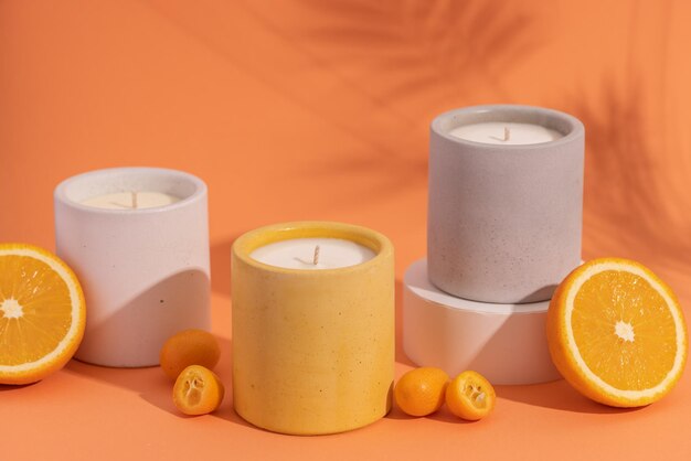 Фото Ароматические соевые свечи премиум-класса в серой бетонной банке на оранжевом фоне с апельсиновыми фруктами и тенью