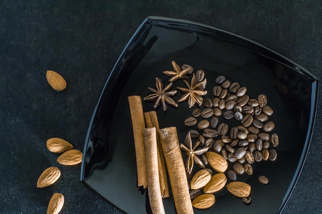 Foto spezie aromatiche con chicchi di caffè e mandorle su fondo nero