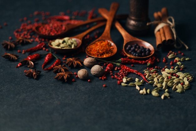 Aromatic spices in wood spoons on dark stone table