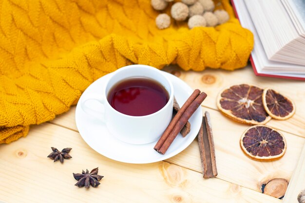 Aromatische hete kaneelthee bedekt met een warme sjaal op een houten herfst achtergrond.