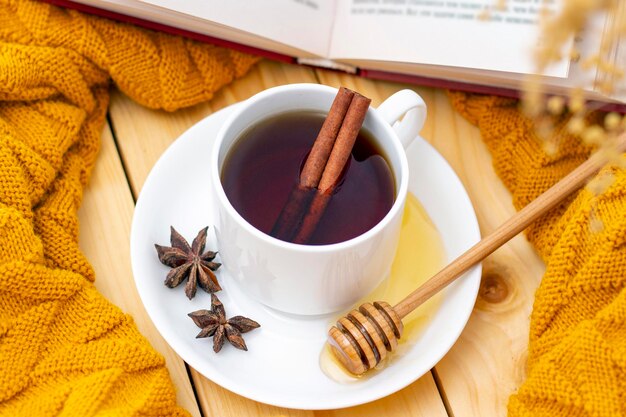 Aromatische hete kaneelthee bedekt met een warme sjaal op een houten herfstachtergrond. honingdipper met honing. comfortabel een boek lezen