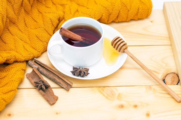 Aromatische hete kaneelthee bedekt met een warme sjaal op een houten herfstachtergrond honingdipper met honing