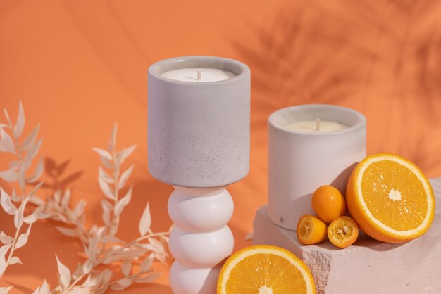 Foto aromatische premium sojakaarsen in grijze betonnen pot op oranje achtergrond met oranje vruchten en schaduw