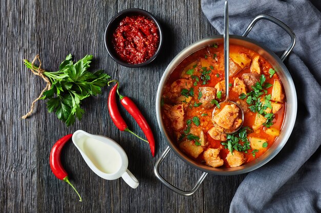 Arrabbiata-stoofpot van kip met linzen en aardappel in een pot op een houten tafel, horizontaal zicht van bovenaf, plat gelegd