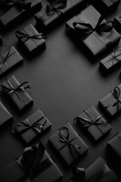 Аранжированные подарочные коробки, завернутые в черную бумагу с черной лентой на черном фоне. Вид сверху. Концепция рождественских праздников. С копией пространства посередине.