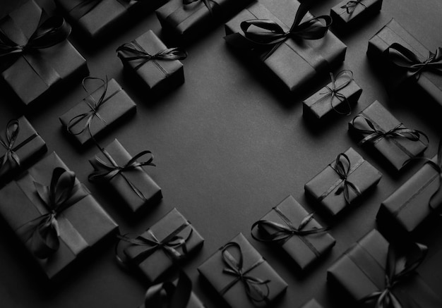 Arranged Gifts boxes wrapped in black paper with black ribbon on black background Top view Christmas holidays concept With copy space in the middle