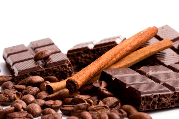 Disposizione di cioccolato, caffè e bastoncini di cannella su bianco