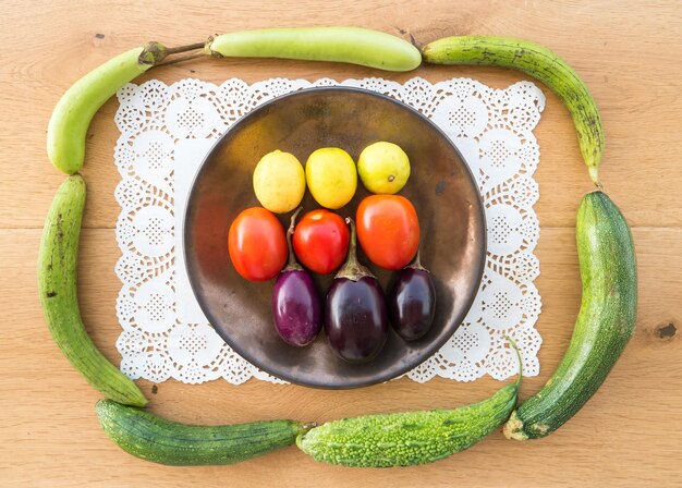 Arrangement of cucumbers surrounding three lemons tomatoes and eggplants on a plate