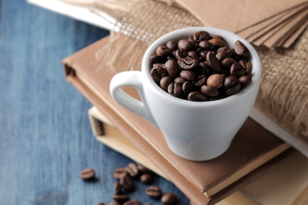 Disposizione con chicchi di caffè in una tazza e libri su un tavolo di legno blu.