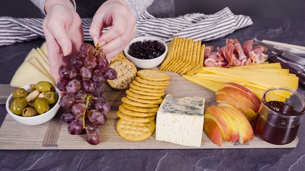 대형 치즈 보드용 보드에 고급 치즈, 크래커 및 과일을 배열합니다.