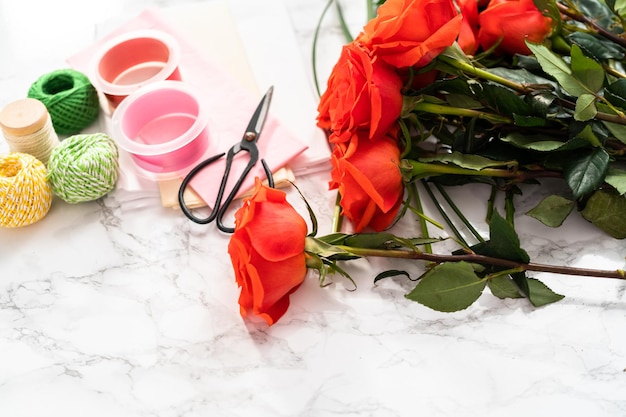 Arranging red roses and green leaves into a bouquet on a marble background.