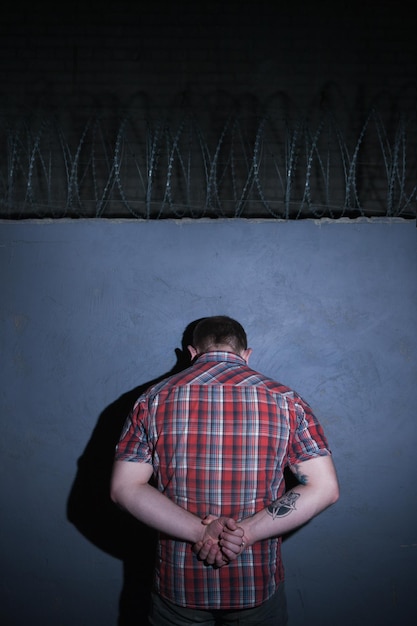 Photo arrested criminal male on blue background detained unrecognizable man with hands behind back punished person at night guilty concept