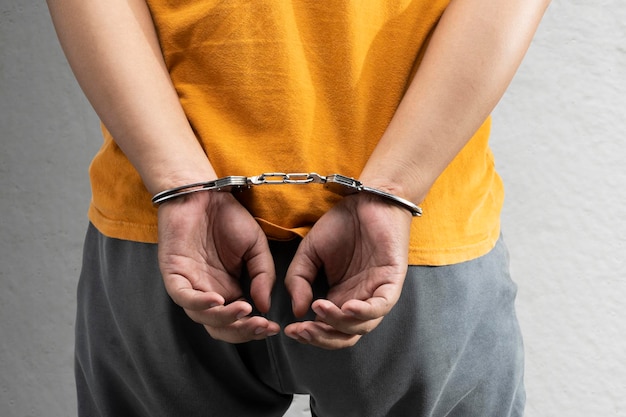 Arrested man with a handcuff on his hand with a gray wall background