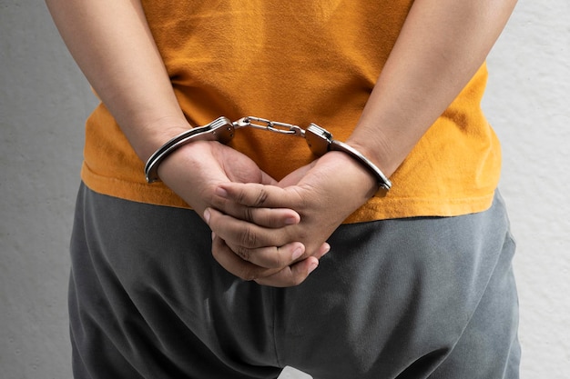 Arrested man with a handcuff on his hand with a gray wall background