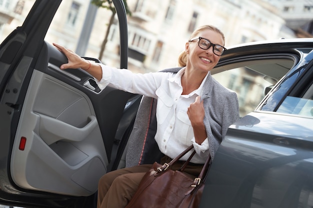 직장에 도착한 행복한 비즈니스 여성은 현대적인 차에서 내리고 웃고 있습니다.