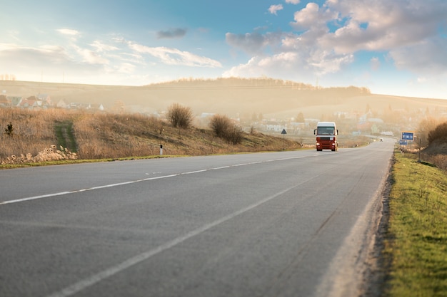 Arriving white truck on the road in a rural landscape at sunset