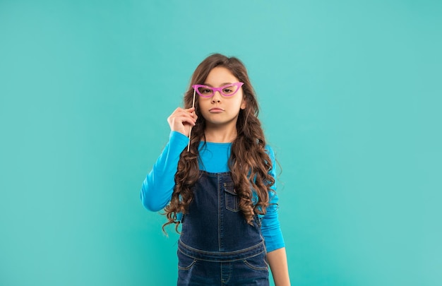 Arrogant kid with long curly hair on blue background funny child with glasses