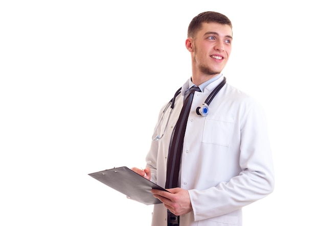 Arrogant young man in white doctor gown with stethoscope on his neck writing in his black folder