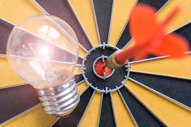 Photo arrow hitting the bullseye target with idea lamp on dartboard