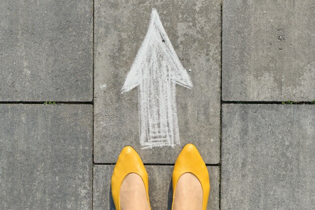 Arrow sign painted on gray sidewalk with womens legs