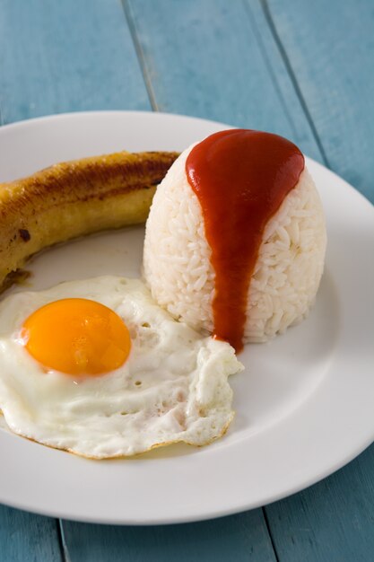 사진 arroz la cubana 튀긴 된 바나나와 나무 테이블에 접시에 튀긴 된 계란 전형적인 쿠바 쌀.