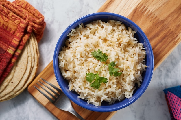 Arroz blanco servido en plato azul sobre tabla de madera con tortillas