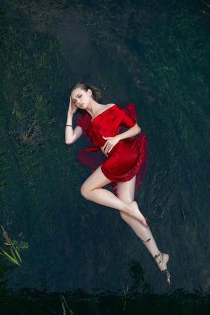 사진 낮 동안 자연에서 여름에 녹색 조류와 함께 강에 누워 빨간 드레스에 섹시 한 젊은 여자의 예술 아름 다운 낭만적 인 초상화