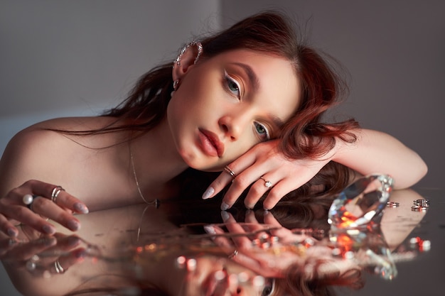 Art beautiful woman with creative makeup is lying on the mirror. Beauty portrait of a romantic woman with jewelry