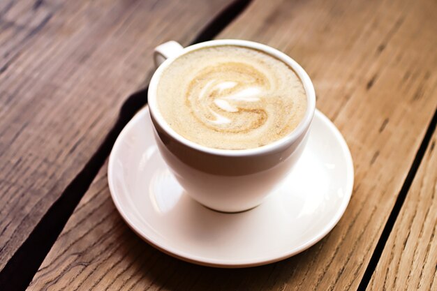 Art cappuccino in the cup on the wooden surface.