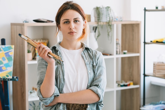 Art class Painting skill improvement Creative hobby Portrait of confident relaxed female artist with paintbrushes in modern light art studio