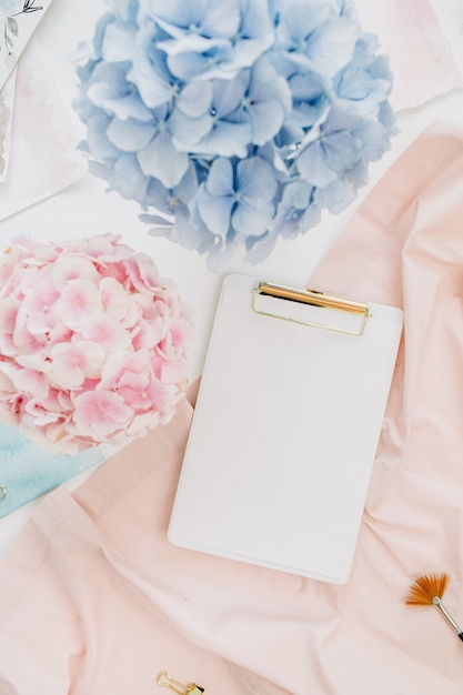 Art composition home office desk workspace with copy space clipboard, pastel hydrangea flowers bouquet, watercolor painting, peachy blanket