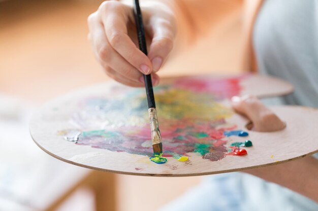 art creativity and people concept close up of artist with palette brush and easel painting at studio