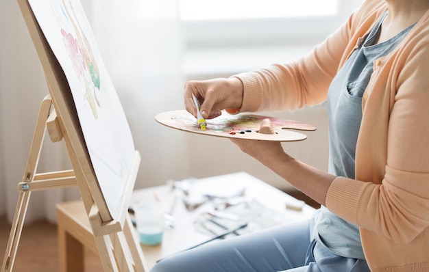 Foto creatività artistica e concetto di persone primo piano dell'artista donna che applica vernice alla palette e dipinge natura morta su cavalletto in studio