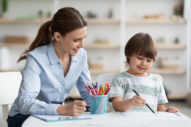 芸術開発の才能のある小さな男の子がカラフルな鉛筆で絵を描く女性心理学者を気遣う