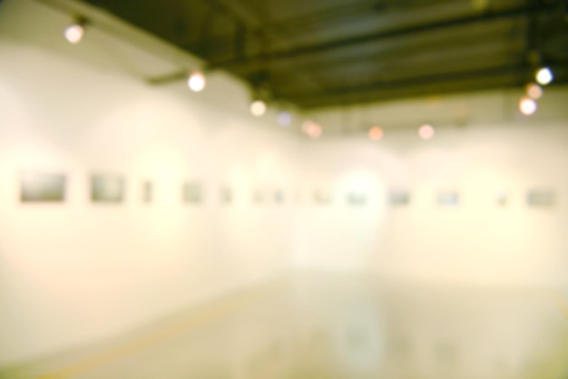 Photo art exhibition gallery blurry background and people looking at paintings on white wall.