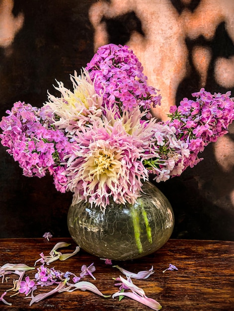 The art of flower arrangement Romantic bouquet with garden phlox and dahlias in a glass vase on a wooden table on an old rusty background in the rays of sunlight