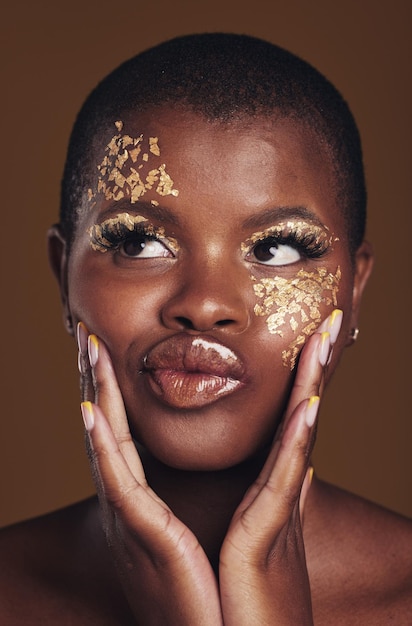 Art fun and black woman in gold makeup on brown background glitter paint or cosmetics Shine glow and silly face of African model in studio for beauty fashion and aesthetic freedom in luxury skin