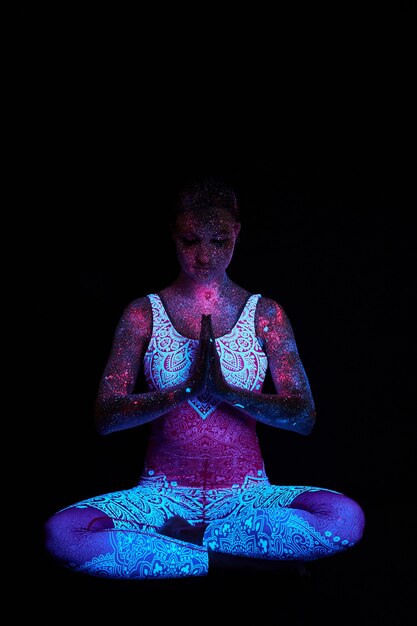 Art girl kosmos in ultraviolet licht. Vrouw doet yoga, lichaamsopwarming. Het hele lichaam is bedekt met gekleurde druppels. Astrale yoga. Ruis, onscherp