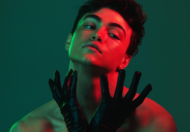 Art neon lights and creative portrait of man with leather gloves serious face and self expression Futuristic cyberpunk fashion topless male model and artistic beauty on green studio background