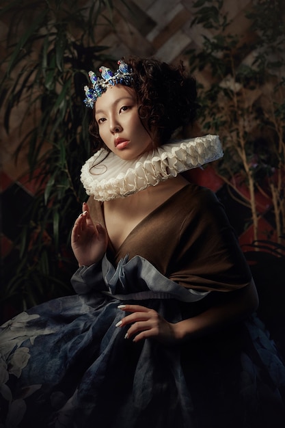 나뭇잎과 녹음이 우거진 소녀 공주 여왕의 예술 초상화, 마법의 드레스를 입은 아시아 여성의 멋진 낭만적인 이미지. 관능적인 부드러운 시선. 궁전의 소녀는 왕자를 기다리고 있습니다