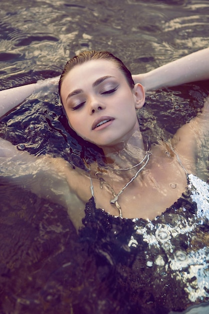 Art portrait of a sexy young mermaid woman lying in the water in a scaly swimsuit