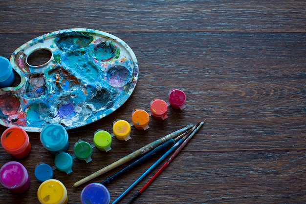 Art set, palette, paint, brushes on wooden background.