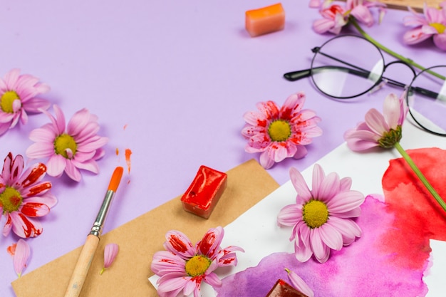 художественные принадлежности, фиолетовые цветы и очки на фиолетовом столе